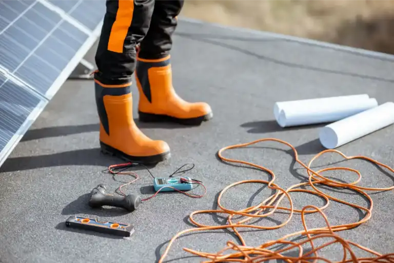 Installing solar panels, close-up on a working tools. wires and man in protective clothing standing on a rooftop with photovoltaic power station